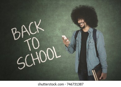 Afor student looking at cellphone while holding book with back to school text on chalkboard 