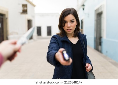 Afraid Caucasian Woman Making Eye Contact And Using A Taser To Defend Herself From A Criminal Thief With A Knife In The Street