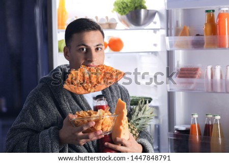 Afraid man caught in the act of choosing tasty food near refrigerator at night