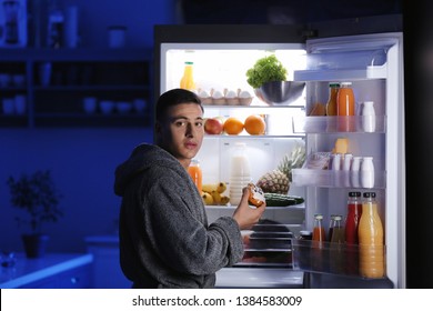 Afraid Man Caught In The Act Of Eating Unhealthy Food Near Refrigerator At Night