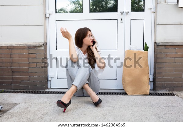 An Afraid Young Woman Sitting Outside The\
Door Talking On Mobilephone