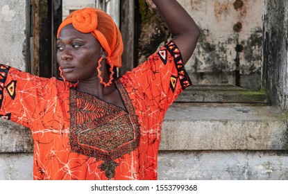 Africa Woman Stands By Old Building With Traditional Orange African Dress. The Place Is From The Colonization Of Takoradi Ghana.