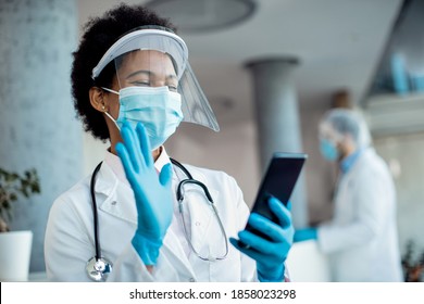 African America Female Doctor Using Mobile Phone And Waiving While Having Video Call From The Hospital During Coronavirus Pandemic. 