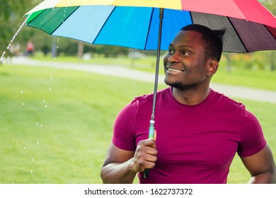African America Man Standing Under Colorful Umbrella In Summer Park Checking For Rain