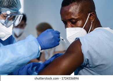 afrikanischer amerikanischer Mann, der sich den Coronavirus covid-19-Syring ansieht, wenn medizinisches Personal Impfstoff gegen Muskeln injiziert, um für ihn eine Immunisierung von Coronavirus covid-19 aufzubauen