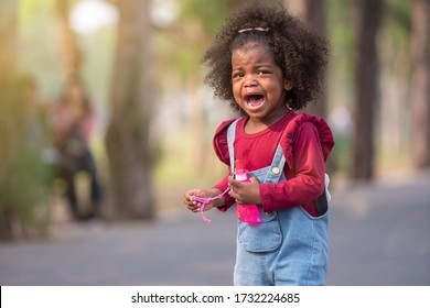 African American adorable kid crying on playground at park. Sad emotion cute afro girl with red t-shirt children's denim bib sets stand alone cry until tears run down. African American child concept.