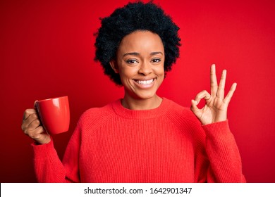 African American afro woman with curly hair drinking cup of coffee over red background doing ok sign with fingers, excellent symbol