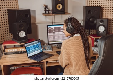 African American anchor woman sitting in front of microphone and laptop with mixing board in recording studio - Powered by Shutterstock