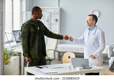 African American Army Officer Leaning On Walking Stick Greeting Mature Caucasian Doctor With Fist Bump