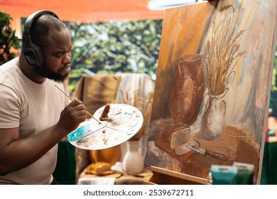 African american artist mixing colors with a paintbrush on a palette and creating a masterpiece on canvas. Skilled male painter working with watercolor and tools in artistic workshop. - Powered by Shutterstock