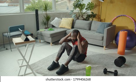 African american athlete performing abdominal core crunches on floor while watching online classes training. Home fitness. Workout. Self-isolation during quarantine. - Powered by Shutterstock