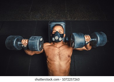 African American Athletic Man In Mask Lifting Dumbbells And Working On His Chest View From Above. Black Man In Gym Doing Exercise For Chest With Dumbbells Close-up