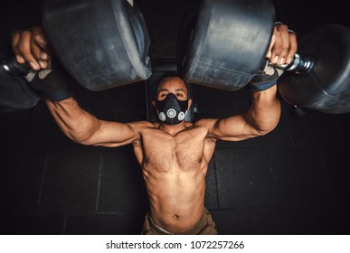 african american athletic man in mask lifting dumbbells and working on his chest view from above. black man in gym doing exercise for chest with dumbbells close-up - Powered by Shutterstock