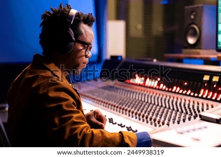 African american audio expert editing tracks in professional recording studio, mixing and mastering music in control room with technical gear. Sound engineer producing new tracks for an album.