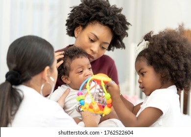 African American Baby Crying Health Examination With Mother Family In Hospital. Pediatrician Doctor Use Stethoscope Check Up Adorable Infant. Cute Girl Kid Help Mum By Cheer Up Baby Sickness With Toy 