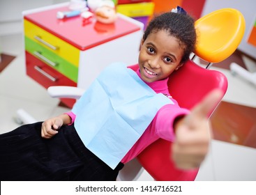 African American baby girl smiling sitting in a dental chair at the examination of the pediatric dentist.