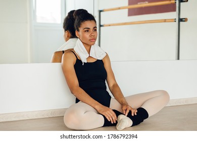 African American Ballet Dancer Relaxing After Training. Young Woman Sitting In Front Of A Mirror In A Dancing Studio.