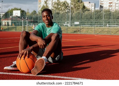 African american basketball player sitting on basketball court relaxing resting after exhausting training showing skills to friends comapny delighted man having break on background guys playing. - Powered by Shutterstock