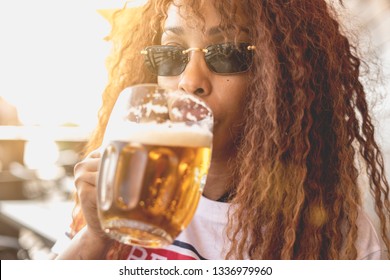 African American beautyful woman drinking a glass of beer on an outdoor summer restaurant