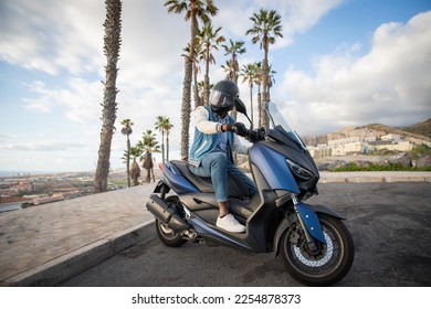 An African American biker sitting on his motorcycle in a tropical location with palm trees - Shutterstock ID 2254878373