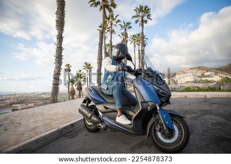 An African American biker sitting on his motorcycle in a tropical location with palm trees