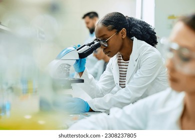 African American biochemist using microscope during scientific research in laboratory. - Powered by Shutterstock