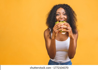 African American black beautiful young woman eating hamburger isolated on yellow background.