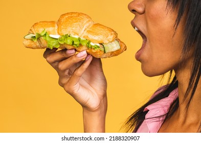 African American Black Beautiful Young Woman Eating Croissant Or Sandwich Isolated Over Yellow Background. Unhealthy Junk Food Diet Concept.