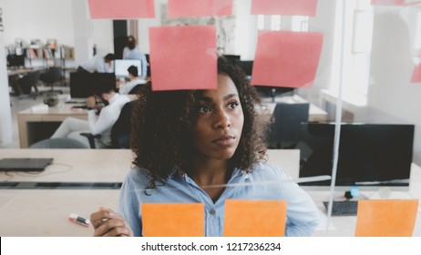 African American black employee looking onto a glass wall with sticky notes, framework for managing work, scrum methodology - Shutterstock ID 1217236234