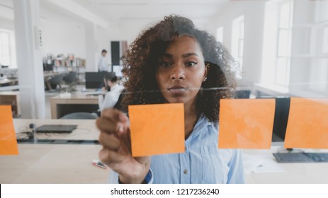 African American black employee looking onto a glass wall with sticky notes, framework for managing work, scrum methodology