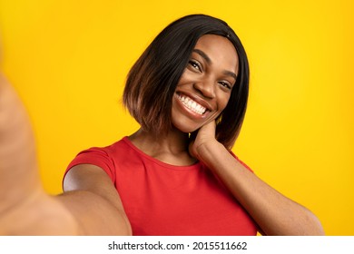 African American Blogger Lady Making Selfie Posing Smiling To Camera In Studio Over Yellow Background, Wearing Red T-Shirt. Self-Portrait Of Cheerful Millennial Woman. Selective Focus