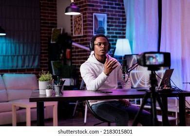 African American Blogger Recording Live Podcast Vlog On Camera, Filming Livestream In Studio With Neon Lights. Social Media Influencer Vlogging Internet Video As Channel Content.