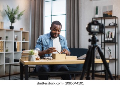 African american blogger unboxing new smartphone and recording video on camera. Young guy sharing with subscribers his feedback about modern gadget.
