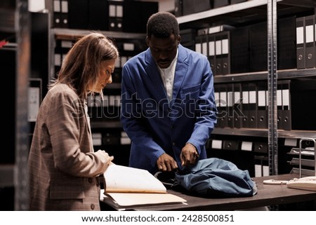 African american bookkeeper preparing to leave office while businesswoman showing bureaucracy record. Diverse depository employees working overtime at administrative record in storage room