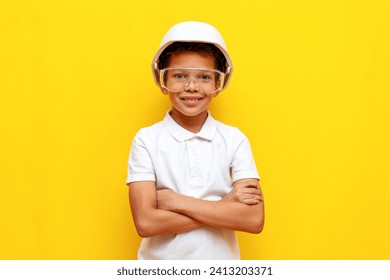 african american boy builder repairman in hard hat and safety glasses stands with crossed arms on blue isolated background, 10 year old child foreman in uniform - Powered by Shutterstock