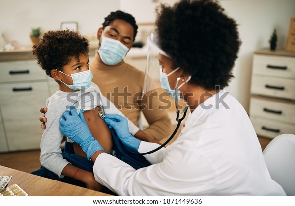 African\
American boy with face mask being examined by female pediatrician\
during medical apportionment at doctor\'s office.\
