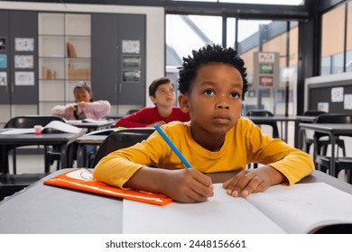 African American boy focused on his schoolwork in a school classroom setting. Biracial girl and another child are in the background, engaged in their studies. - Powered by Shutterstock