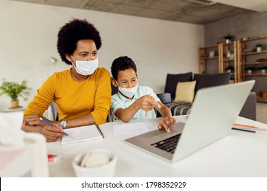 African American Boy And His Mother Wearing Face Masks And Using Laptop While Learning At Home During COVID-19 Epidemic. 