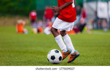 African American Boy In Junior Football Team Leading Ball On Grass Training Field. Youth Soccer Player Kicking Ball