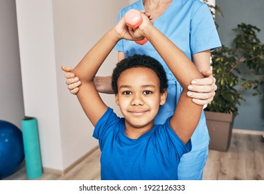 African American Boy Lifts Dumbbells, Physical Therapist Helps Exercise Properly To Rehabilitation Child Health