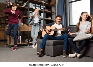 African American Boy Playing Acustic Guitar While His Friends Dancing Behind At Home, Teenagers Playing Guitar Concept