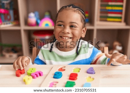 African american boy playing with maths puzzle game sitting on table at kindergarten