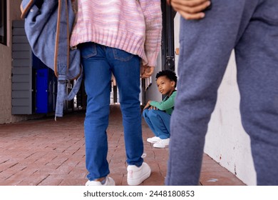 African American boy sits crouched between other children in school, looking sad. His gaze is directed upwards, capturing a moment of curiosity or concern amidst an urban setting. - Powered by Shutterstock