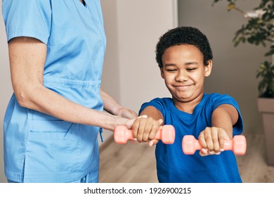 African American boy trains with physiotherapist using dumbbells at rehab center