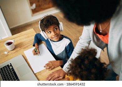 African American boy wearing headphones while homeschooling and communicating with his mother.  - Powered by Shutterstock