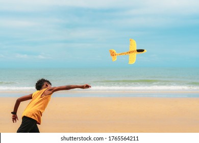 African American boy in yellow tank top fly airplane toy at the beach under blue sky. Concept for dream job, summer vacation and travel , and childhood.