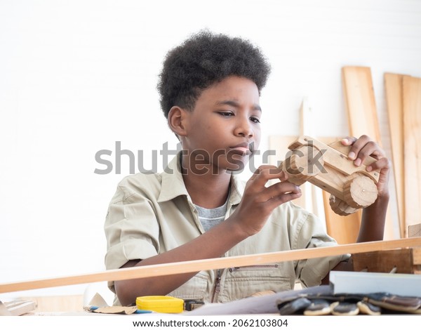 African American boys are deliberately examining a\
piece of a wooden toy car ordered by their teacher during their\
online class.
