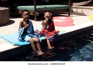 African american brother and sister eating ice creams while sitting at poolside at resort in summer. Unaltered, family, love, togetherness, childhood, food, enjoyment and weekend concept. - Powered by Shutterstock