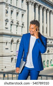 African American Business Man With Little Goatee, Working In New York, Wearing Blue Suit, White T Shirt, Standing By Office Building, Holding Laptop Computer, Talking On Phone.