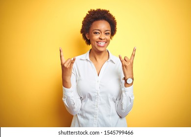 African American Business Woman Over Isolated Yellow Background Shouting With Crazy Expression Doing Rock Symbol With Hands Up. Music Star. Heavy Music Concept.